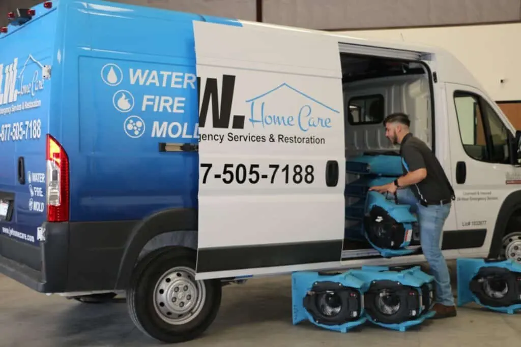 JW Home Care technician loading air movers and drying equipment into a company van